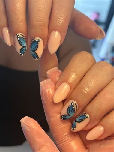 Nude almond nails with blue butterfly designs.